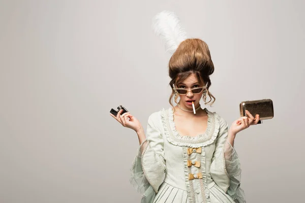 Молода жінка в ретро вбрання тримає легший і золотий гаманець під час куріння ізольовані на чорному — стокове фото