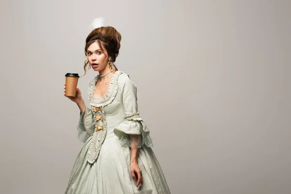 Surprised woman in vintage outfit holding paper cup while looking at camera isolated on grey — Stock Photo