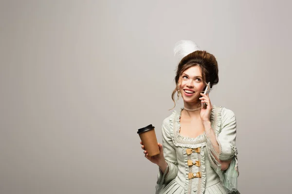 Femme heureuse en robe vintage élégante parlant sur smartphone tout en tenant tasse en papier isolé sur gris — Photo de stock