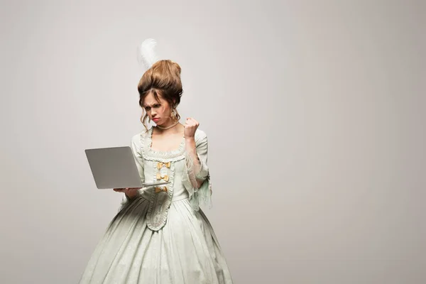 Mulher zangada em roupa retro mostrando punho apertado perto do computador isolado em cinza — Fotografia de Stock