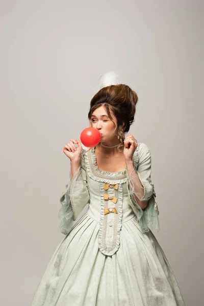 Bonita mujer en vestido retro soplado goma de mascar roja aislada en gris - foto de stock