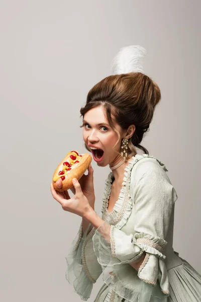 Mujer elegante en vestido vintage elegante comer hot dog aislado en gris - foto de stock