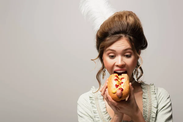 Jeune femme en tenue rétro mordant délicieux hot dog isolé sur gris — Photo de stock