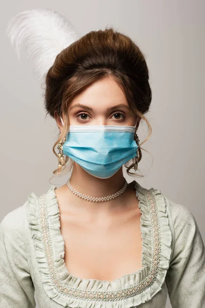 Jeune femme élégante en tenue vintage et masque médical regardant la caméra isolée sur gris — Photo de stock