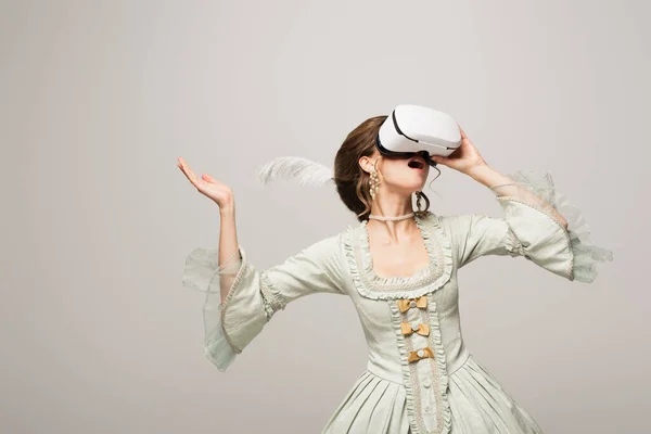 Mulher surpreso em elegante vestido vintage jogos em vr fone de ouvido isolado em cinza — Fotografia de Stock