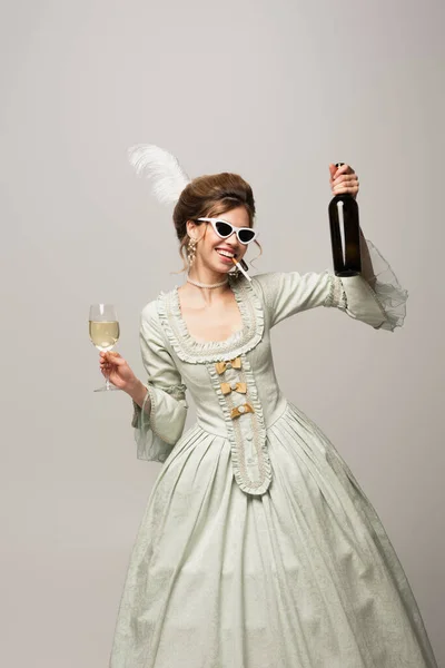 Mujer alegre en traje vintage posando con vino y cigarrillo aislado en gris - foto de stock