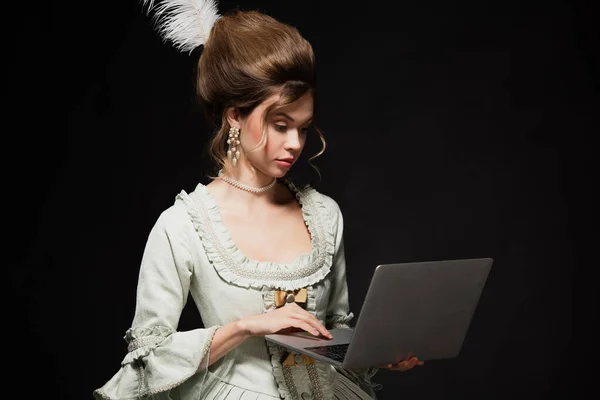 Charming woman in vintage outfit typing on laptop isolated on black — Stock Photo