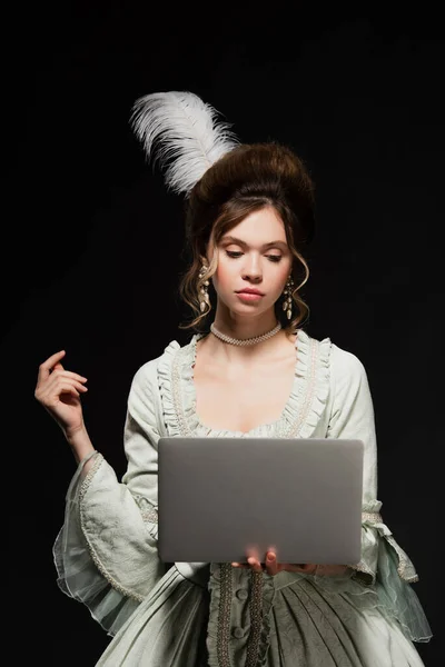 Affascinante donna in elegante abito vintage guardando computer portatile isolato su nero — Foto stock