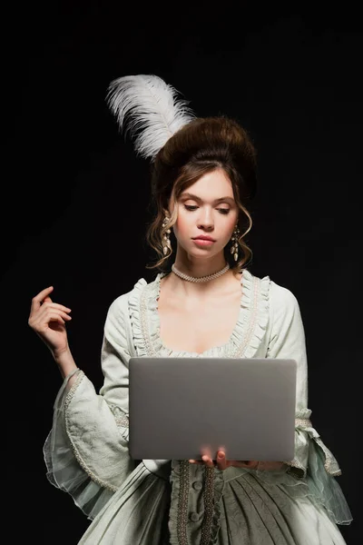 Mujer encantadora en traje vintage elegante mirando portátil aislado en negro — Stock Photo