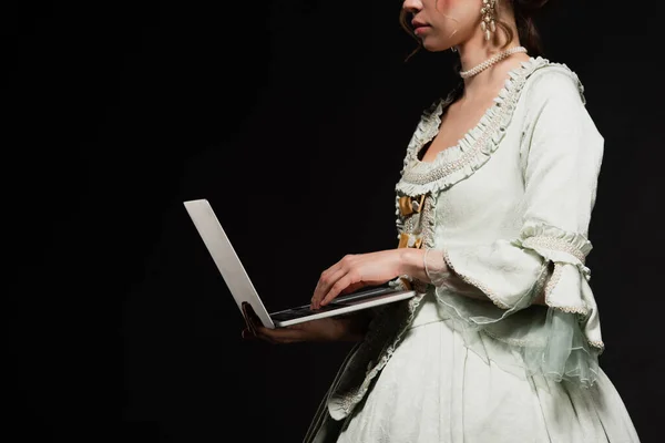 Partial view of young woman in elegant vintage dress using laptop isolated on black — Stock Photo