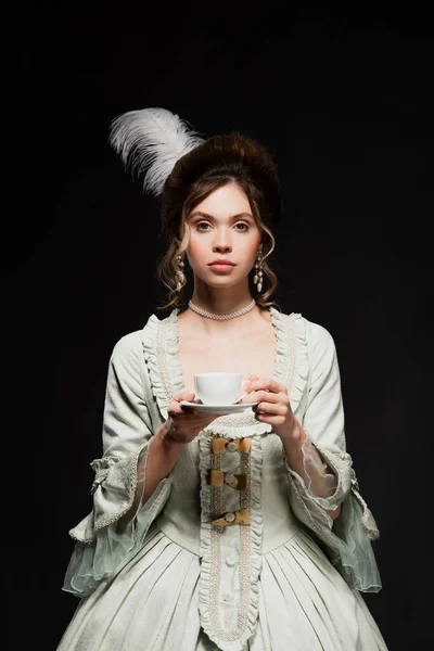 Чарівна жінка в старовинній пастельній сірій сукні, що тримає чашку кави ізольовано на чорному — стокове фото