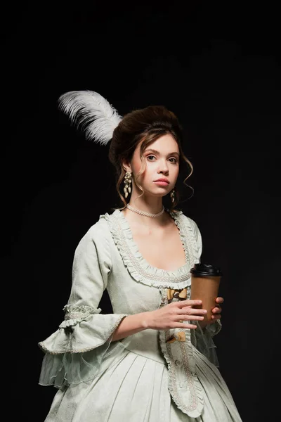 Charmante femme de style vintage avec tasse jetable regardant la caméra isolée sur noir — Photo de stock