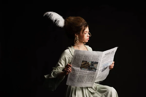 Elegante mujer en vestido vintage gris pastel leyendo viaje vida periódico aislado en negro - foto de stock