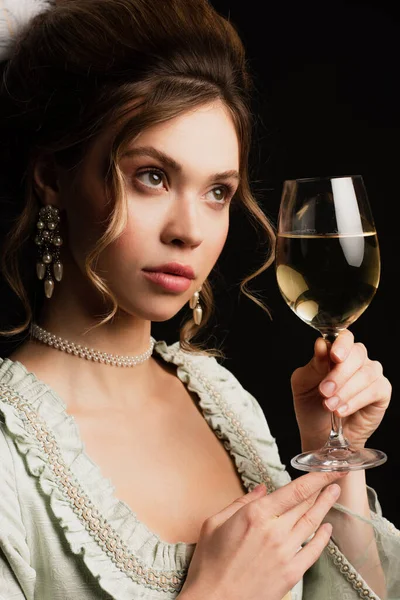 Mujer encantadora en elegante traje vintage sosteniendo copa de vino blanco aislado en negro - foto de stock