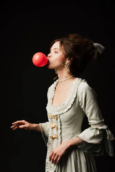 Jeune femme en robe vintage élégante soufflant chewing-gum isolé sur noir — Photo de stock