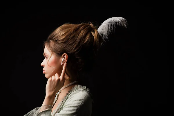 Вид збоку жінка в ретро-стилі вказує на навушники під час прослуховування музики ізольовано на чорному — стокове фото
