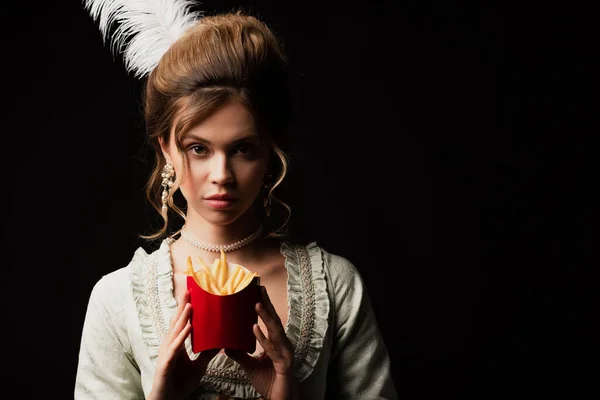 Bonita, mulher estilo retro olhando para a câmera enquanto segurando batatas fritas isoladas em preto — Fotografia de Stock