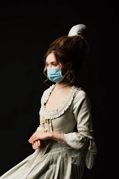 Mujer de estilo vintage en máscara médica sentado aislado en negro - foto de stock