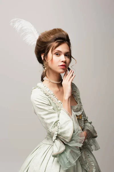 Mujer encantadora en elegante traje retro posando con la mano cerca de la cara aislada en gris - foto de stock