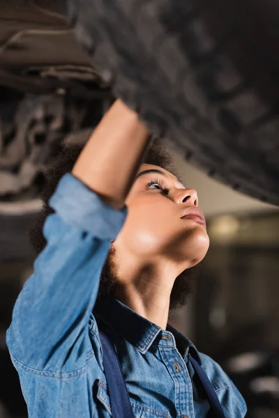 Vista da vicino del giovane meccanico afroamericano che ripara il fondo dell'auto in garage — Foto stock