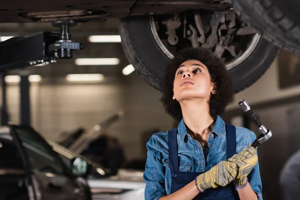 Young african american mechanic repairing bottom of car in garage — Stock Photo