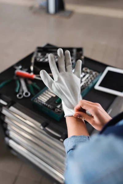 Teilansicht des jungen Mechanikers mit Handschuhen in der Nähe von Werkzeugkiste und digitalem Tablet im Autoreparaturservice — Stockfoto