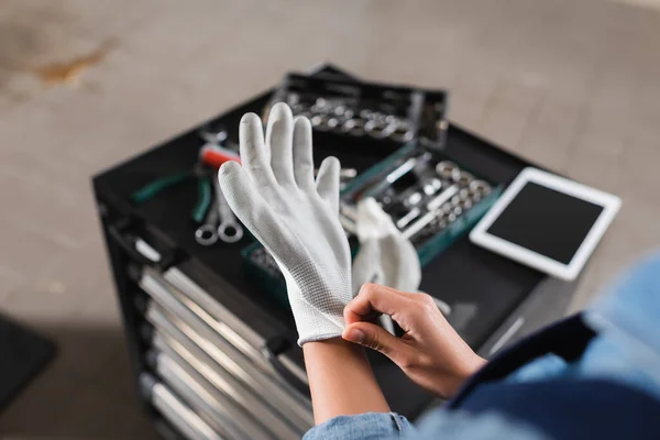 Teilbild des jungen Mechanikers mit Handschuhen in der Nähe von Werkzeugkiste und digitalem Tablet in der Garage — Stockfoto