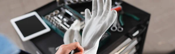 Ausgeschnittene Ansicht eines jungen Mechanikers mit Handschuhen in der Nähe von Werkzeugkiste und digitalem Tablet in der Garage, Banner — Stockfoto
