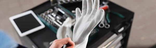 Vista ritagliata del giovane meccanico che indossa guanto a portata di mano vicino alla cassetta degli attrezzi e tablet digitale in garage, banner — Foto stock