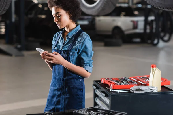 Junger afrikanisch-amerikanischer Mechaniker chattet mit Handy in Garage — Stockfoto