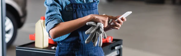 Cropped view of young african american mechanic typing on cellphone in garage, banner — Stock Photo