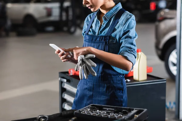 Teilansicht eines jungen afrikanisch-amerikanischen Mechanikers, der in der Garage auf dem Handy tippt — Stockfoto