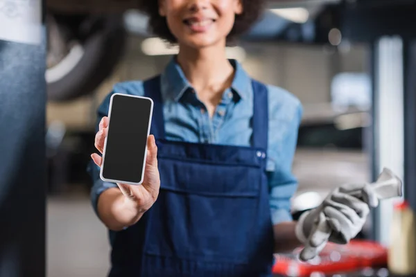 Vista parziale del cellulare in mano del giovane meccanico afroamericano sfocato in garage — Foto stock