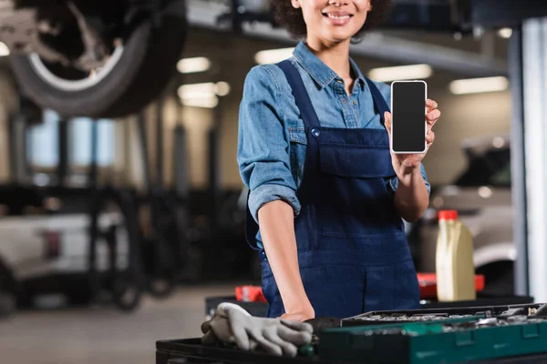 Cropped view of young african american mechanic showing cellphone with blank screen in garage — Stock Photo