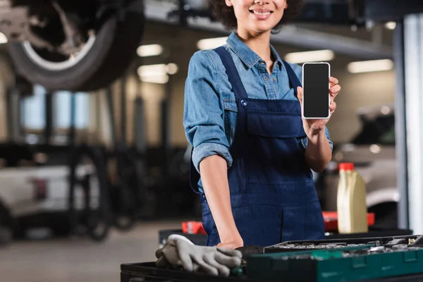 Vue recadrée du jeune mécanicien afro-américain montrant téléphone portable avec écran blanc dans le garage — Photo de stock