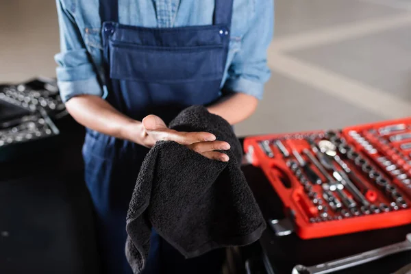 Vista parcial de joven afroamericano mecánico en overoles secado manos con toalla en garaje — Stock Photo