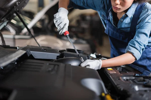 Vista parcial del joven mecánico afroamericano sosteniendo destornillador y la fijación de motor de coche en el garaje - foto de stock