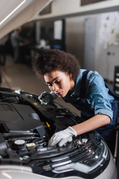 Junger afrikanisch-amerikanischer Mechaniker hält Schraubenschlüssel und fixiert Automotor in Garage — Stockfoto