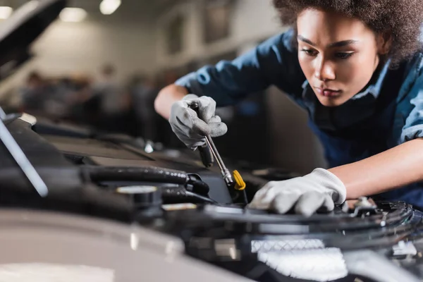 Young african american mechanic working with motor of car in garage — Stock Photo