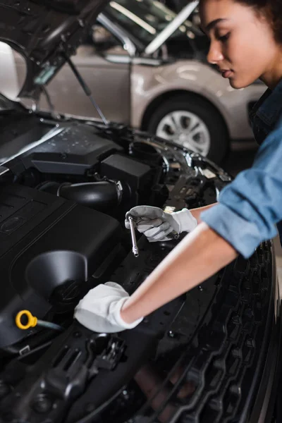 Junger afrikanisch-amerikanischer Mechaniker hält Schraubenschlüssel-Befestigungsmotor in Auto mit offener Motorhaube in Garage — Stockfoto