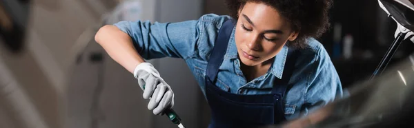 Jovem afro-americano mecânico trabalhando com instrumento na garagem, banner — Fotografia de Stock