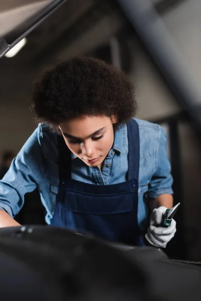 Jovem afro-americano mecânico segurando alicates e trabalhando com motor de carro na garagem — Fotografia de Stock