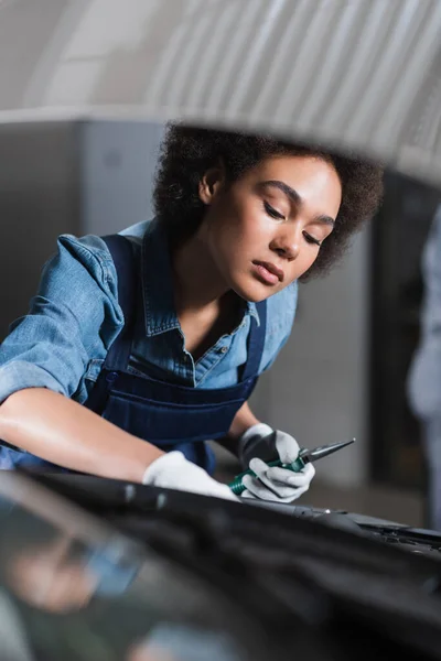 Junger afrikanisch-amerikanischer Mechaniker hält Zange und fixiert Auto-Motor in Garage — Stockfoto