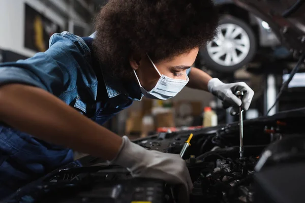 Junger afrikanisch-amerikanischer Mechaniker in Schutzmaske arbeitet mit dem Auto in der Garage — Stockfoto