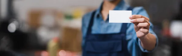 Close up view of empty card in hand of blurred young african american mechanic in garage, banner — Stock Photo