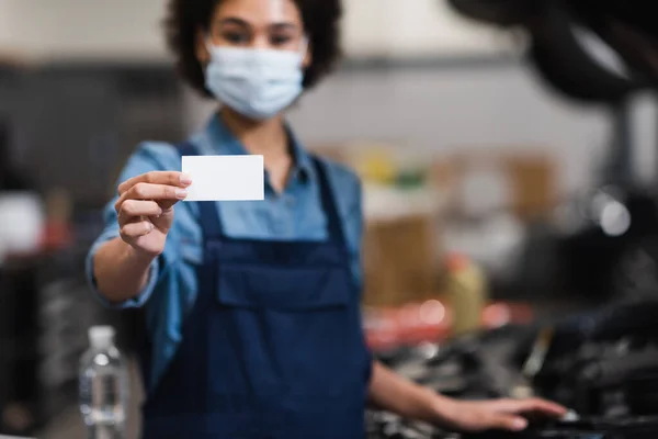 Leere Karte in der Hand eines verschwommenen jungen afrikanisch-amerikanischen Mechanikers mit Schutzmaske in der Garage — Stockfoto