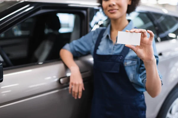 Vue partielle du jeune mécanicien afro-américain montrant la carte vide et debout près de la voiture dans le garage — Photo de stock