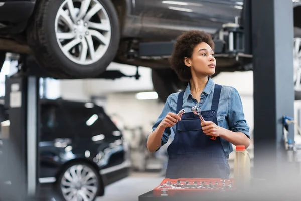 Junger afrikanisch-amerikanischer Mechaniker hält Ausrüstung in der Nähe des Werkzeugkastens in der Garage — Stockfoto