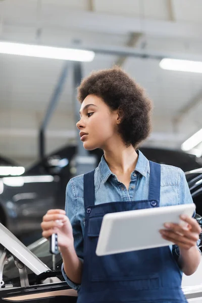 Jovem afro-americano mecânico em macacão segurando chave de carro e tablet digital na garagem — Fotografia de Stock