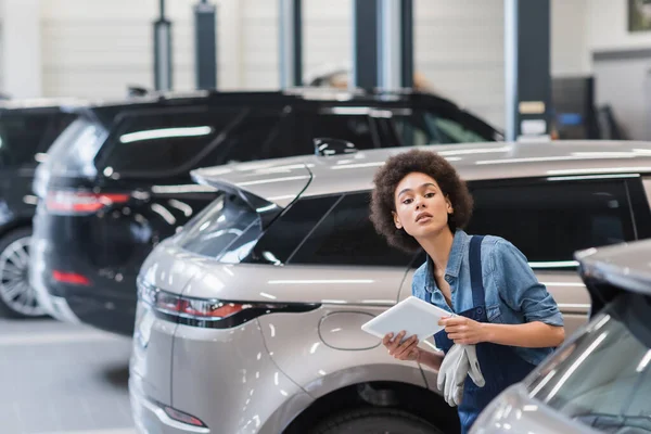 Joven afroamericano mecánico chequeo de coches con tableta digital en garaje - foto de stock